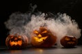 Three creepy Halloween grinning pumpkins glow in the dark among the fog. jack-o-lantern in a witch hat on a black
