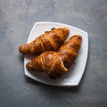 Three croissants and one bitten in a white saucer on a gray concrete background. Royalty Free Stock Photo