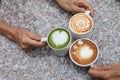 Three cup of different coffee which are cappucino, mocha latte and caramel milk holding by hand of friend on the rustic table