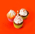 Three cupcakes with a candle cream on an orange background Royalty Free Stock Photo