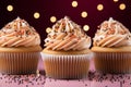 three cupcakes with frosting and sprinkles on a pink background