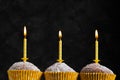 Three cupcakes in paper cups with yellow candles with flame surprise birthday on a low key