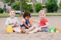 Three cute Caucasian and hispanic latin toddlers babies children sitting in sandbox playing with plastic colorful toys Royalty Free Stock Photo