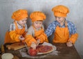 Three cute European boys dressed as cooks are busy cooking pizza. three brothers help my mother to cook pizza Royalty Free Stock Photo