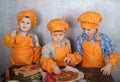 Three cute European boys dressed as cooks are busy cooking pizza. three brothers help my mother to cook pizza Royalty Free Stock Photo