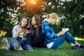 Three cute girls relax and socialize on the lawn in the summer park. Young women on the green grass among the trees, looking