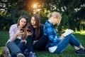 Three cute girls relax and socialize on the lawn in the summer park. Young women on the green grass among the trees, looking