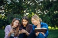 Three cute girls relax and socialize on the lawn in the summer park. Young women on the green grass among the trees, looking