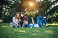 Three cute girls relax and socialize on the lawn in the summer park. Young women on the green grass among the trees, looking