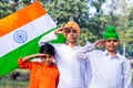 Three cute little Indian kids holding and saluting Tricolor flag near a lake with greenery in the background. Royalty Free Stock Photo