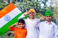 Three cute little Indian kids holding and saluting Tricolor flag near a lake with greenery in the background. Royalty Free Stock Photo