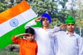 Three cute little Indian kids holding and saluting Tricolor flag near a lake with greenery in the background. Royalty Free Stock Photo