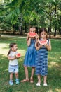 Three cute little sisters eating watermelon in park in summertime