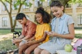 Cute multicultural schoolkids using smartphones while sitting on bench in schoolyard