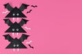 Three cute paper vampire bats with funny googly eyes on side of pink Halloween background with copy space
