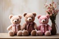 Three cute teddy bears in brown and pink colors with bows sit on a wooden surface with flowers in the background on a Royalty Free Stock Photo