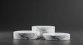 Three cylindrical marble platforms are arranged on a smooth, dark gray surface