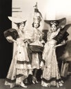 Three dancers in long dresses and large hats