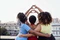 Three dark-skinned young women show heart symbols with their hands. African girls in casual clothes are standing on roof of house Royalty Free Stock Photo