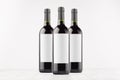 Three dark wine bottles with blank white labels on white wooden board, mock up.