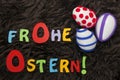 Three decorated Easter eggs and colorful letters saying `Happy Easter` in German on brown shag.