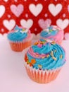 Three delicious chocolate and vanilla cupcakes  with colorful frosting and sprinkles on a pink and red hearts background Royalty Free Stock Photo