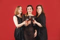 Three delighted women in black dress with red wine glasses over red background. Women party Royalty Free Stock Photo