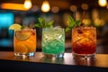 Three different colored cocktails on the bar counter with ice spread around and a shallow depth of field of the bar