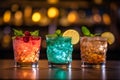 Three different colored cocktails on the bar counter with ice spread around and a shallow depth of field of the bar