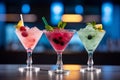 Three different colored cocktails on the bar counter with ice spread around and a shallow depth of field of the bar