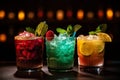 Three different colored cocktails on the bar counter with ice spread around and a shallow depth of field of the bar