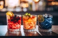 Three different colored cocktails on the bar counter with ice spread around and a shallow depth of field of the bar