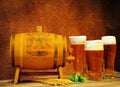 Three different glasses of light beer with foam, a wooden barrel, ears of wheat and fruits of hops on a wooden table against a Royalty Free Stock Photo
