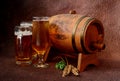 Three different glasses with light beer, next to a wooden barrel, hops and barley ears on a brown abstract background Royalty Free Stock Photo