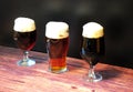 Three different glasses with a third of different types of dark beer are in a row on a wooden table Royalty Free Stock Photo