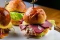 Three different mini burgers set on a wooden tray