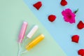 Three different tampons in front of a pink petunia flower and red rose petals. Hygiene products for women. Top view