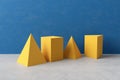 Three-dimensional yellow prism pyramid and rectangular cube objects on blue colored background
