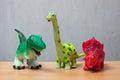 Three dinosaurs toys standing on a wooden floor.