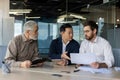 Three diverse business people talking together sitting at a meeting desk inside office, businessmen in business suits Royalty Free Stock Photo