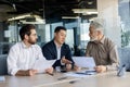 Three diverse business people talking together sitting at a meeting desk inside office, businessmen in business suits Royalty Free Stock Photo