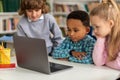 Three diverse kids exploring on laptop in classroom