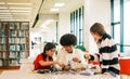 Three diverse students African, Indian, and Asian collaborate on a robotics project at a library table, surrounded by books Royalty Free Stock Photo