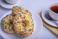 Three donuts coated with yellow icing with sprinkles and cup of coffee on the table