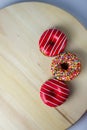 Three donuts of different colors lie on a wooden stand.