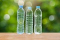 Three drinking water bottles on wooden table on blurred green bokeh background