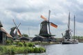 Three dutch mills with orange wings near the canal with one beautiful boat under the cloudy sky