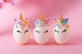 Three Easter eggs in the form of a unicorn with golden corn and flowers on a pink background. Royalty Free Stock Photo