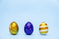 Three easter trendy colored classic blue and golden decorated eggs striped pattern on blue. Happy Easter card with copy