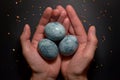 Three eggs, painted hibiscus tea on a black background, in men`s palms and crumbs of sugar glaze, like a dragon egg Royalty Free Stock Photo